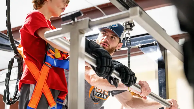 A coach steadies a young skater in the safety harness on the skating treadmill
